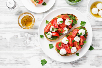 Bruschetta with cherry tomatoes, mozzarella cheese and pesto sauce on wooden board. Traditional...