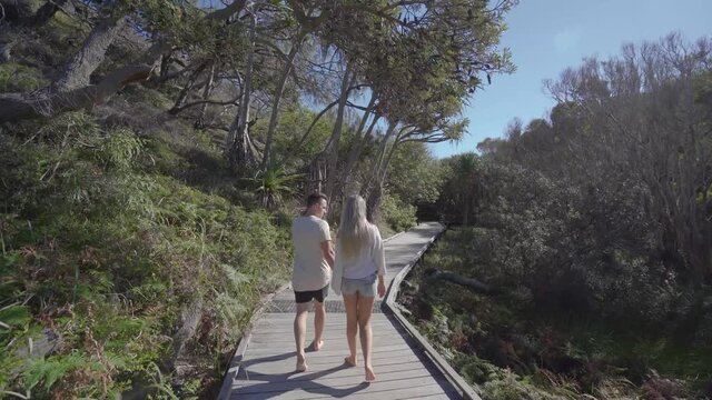  Young Couple Walking on nature boardwalk at Eli Creek, Fraser Island - wide shot following from behind