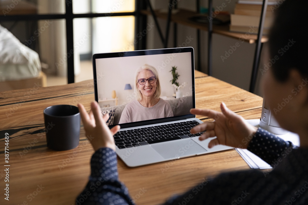 Poster Rear view of female student talk speak on video call on computer with mature Caucasian teacher ort tutor. Woman have webcam conference or virtual digital event with middle-aged coach at home.