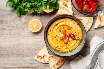 Roasted red pepper hummus with pita bread on wooden background. top view	