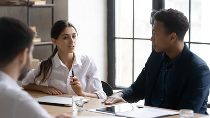 Focused multiracial colleagues gather in boardroom talk discuss business ideas at meeting together. Concentrated diverse multiethnic employees talk brainstorm at briefing in office. Teamwork concept.