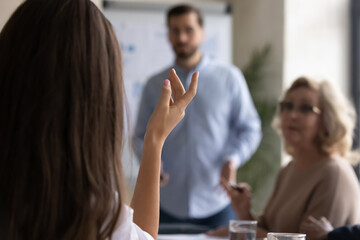 Crop close up of confident female employee raise hands ask answer question at business meeting in office. Woman volunteer interact with coach, participate in team group discussion at briefing.