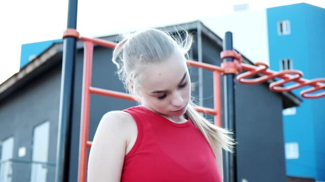 young fit blond busty woman with ponytail in red top stretches neck at sports ground. Healthy lifestyle, wellness. caucasian slim female in sportswear working out, fitness training outdoors at yard