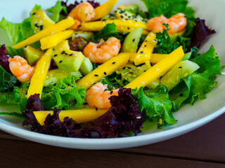 appetizing salad of shrimp, mango, avocado, cucumber, mix of lettuce leaves, decorated with black sesame seeds, on a white plate, close-up
