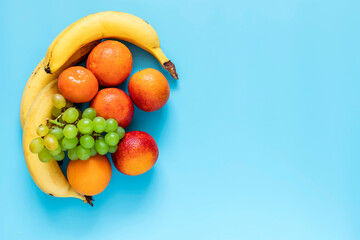 Oranges, bananas and grapes on blue background. Healthy and fresh fruits. Top view.