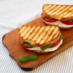 Tasty Grilled Caprese Panini (Mozzarella, Tomatoes and Basil) on a rustic wooden board, side view.
