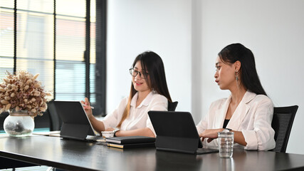 Two businesswomen employees colleagues are explaining new online idea for their startup business in office.