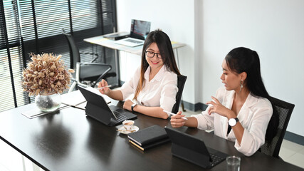 Two businesswomen employees colleagues discussing working together on digital tablet.