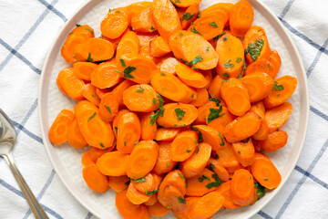 Homemade Sauteed Carrots on a plate on a white wooden surface, top view. Flat lay, overhead, from above.