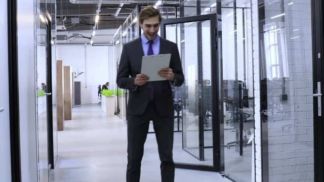 Joyful businessman reading a good financial report walks around in the open space office hallway.