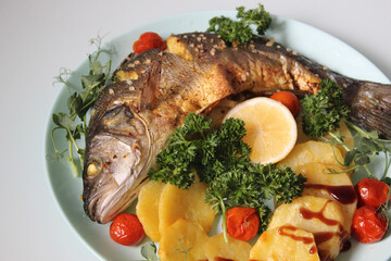 Fried fish with potatoes and decorated with lettuce and lemon on a light background