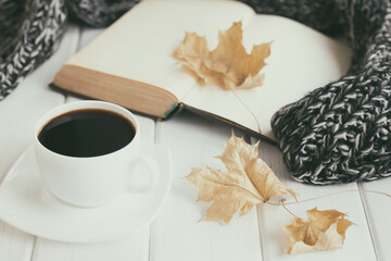 Autumn leaves, cup of coffee, warm knitted scarf and open old book. Cozy home reading concept. Retro nostalgic mood