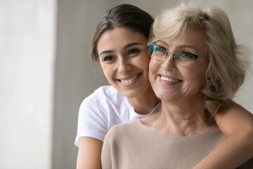Smiling senior mother and adult daughter hug cuddle look in distance dream think of happy future. Optimistic mature mom and grownup girl child embrace visualize at home, enjoy tender family moment. © fizkes