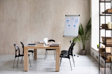 Modern loft office workplace with wooden conference table with document laptop on, whitebeard with diagrams prepared from presentation. Empty boardroom with desk for group briefing or meeting.