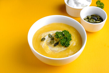 Bowl of pumpkin soup with green leaf at the yellow background
