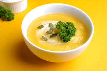 Bowl of pumpkin soup with green leaf at the yellow background
