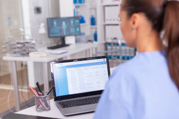Medical nurse checking patient documentation on laptop in hospital office. Health care physician using computer in modern clinic looking at monitor, medicine, profession, scrubs.
