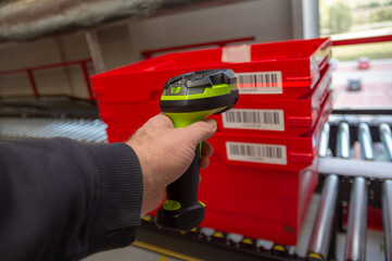 man holds a scanner and scans a barcode on a plastic box