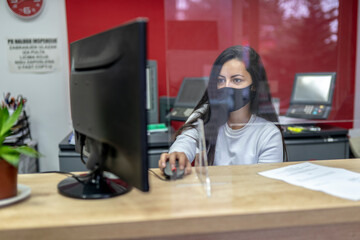Fototapeta na wymiar Beautiful woman wearing face mask and using computer in copy shop