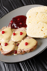 Svickova na smetane is a traditional Czech dish made with beef sirloin and vegetables served with cranberry jam and dumplings close-up in a plate on the table.  vertical
