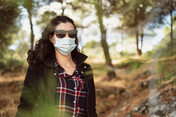 An attractive woman in sunglasses and a mask looks at camera with sunglasses