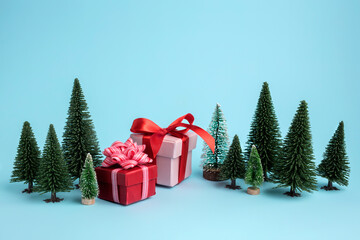 Christmas scene made with miniature pine trees, wrapped gifts and ornaments on blue background. Minimal New Year celebration or winter season concept. Greeting card.