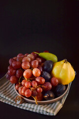 Fresh grapes, pear, apple and plums on a black background. Fruits in a plate .Free space for text.