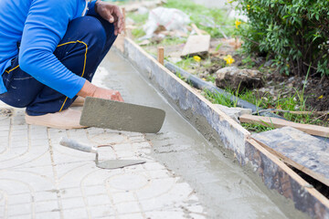 Worker, labor or mason is sitting and repairing or constructing walkway or pathway by using trowel plastering touch cement concrete. Concept of working at construction site.