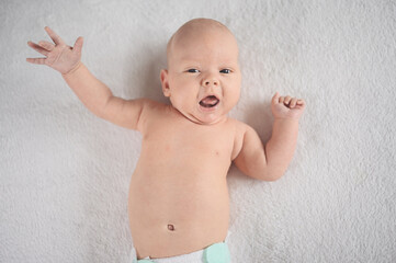 Cute emotional smiling funny newborn boy laying on bed top view. Baby facial expressions.