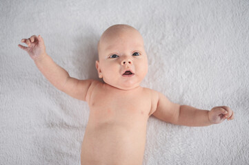 Cute emotional smiling funny newborn boy laying on bed top view. Baby facial expressions.