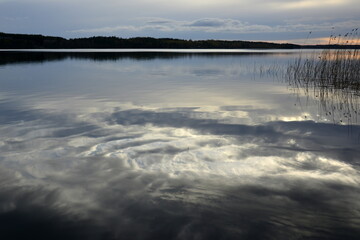 Mirror water surface reflecting sunlit clouds in evening