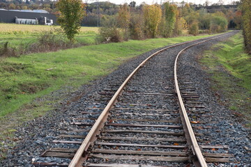 Fototapeta premium Voie de chemin de fer unique avec traverses en bois de type vignole, au milieu de la campagne en automne, ville de Saint Quentin Fallavier, département de l'Isère, France