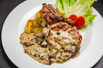 Grilled pork meat on the bone with mushroom sauce, green peas, potato and cherry tomato