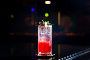A layered red and transparent long drink cocktail in a collins highball glass, with ice, garnished with mint and marshmallow