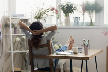 Back view of calm woman florist or decorator sit relax lean in chair relieve negative emotions. Female designer rest at workplace, daydream or take nap break. Stress free, relaxation concept.