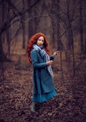 Lonely calm girl with red hair in a gray coat in a spring forest