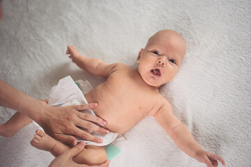 Mother is changing diaper for cute emotional funny newborn little infant baby boy laying in crib