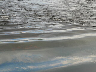 Ripple on the gray water surface, Wave in the sea and the reflection of the blue sky and white cloud