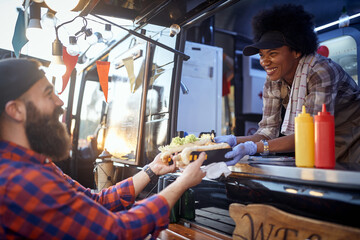 polite female employee holding, giving, two sandwiches to a satisfied beardy customer