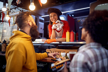 young male is about to eat sandwich in front of fast food service, looking at satisfied employee smiling