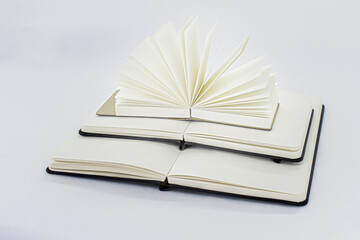 Two unfold notebooks lie on top of each other and fan open notepad with blank light beige pages. Pyramid of books. White background