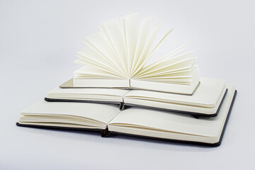 Three unfold notebooks lie on top of each other. Small fan open notepad with blank light beige pages. Pyramid of books. White backdrop