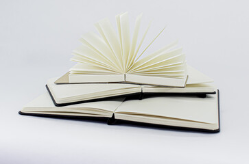 Two unfold notebooks lie on top of each other and fan open notepad with blank light beige pages. Pyramid of books. White backdrop
