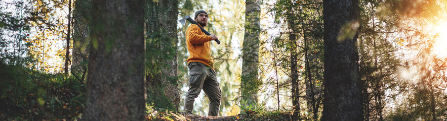 Strong bearded lumberman wearing work clothes holds axe on his shoulder. Wide image