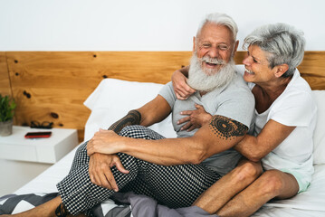 Happy senior couple smiling together in bed - Hipster mature people having funny bed time - Elderly...