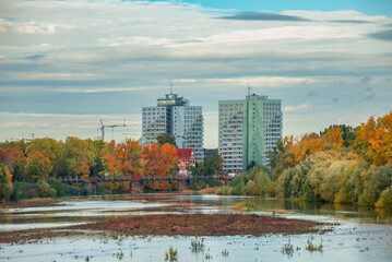 Fototapeta premium Panoramic view over multistore living houses, construction cranes, Elbe river creek and city park nature at colorful golden Autumn, Germany.