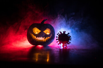 Halloween during Corona virus global pandemic concept. Glowing pumpkins and Covid novel on dark with thematic spooky decorations. Halloween pumpkin on foggy backlight.