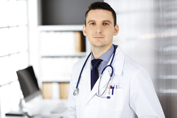 Male doctor standing straight in clinic near his working place. Perfect medical service in hospital. Medicine and healthcare concept