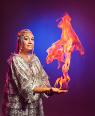 Fairy in a white festive new year costume lights a flame on her hand in the studio