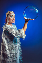 Fairy in a white festive new year costume blows soap bubbles in the studio